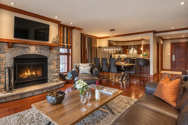 A spacious living room with a stone fireplace, leather furniture, a dining area, and a kitchen in the background.