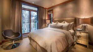 Une chambre à coucher avec un grand lit, une chaise, une table de chevet et une fenêtre avec des rideaux.