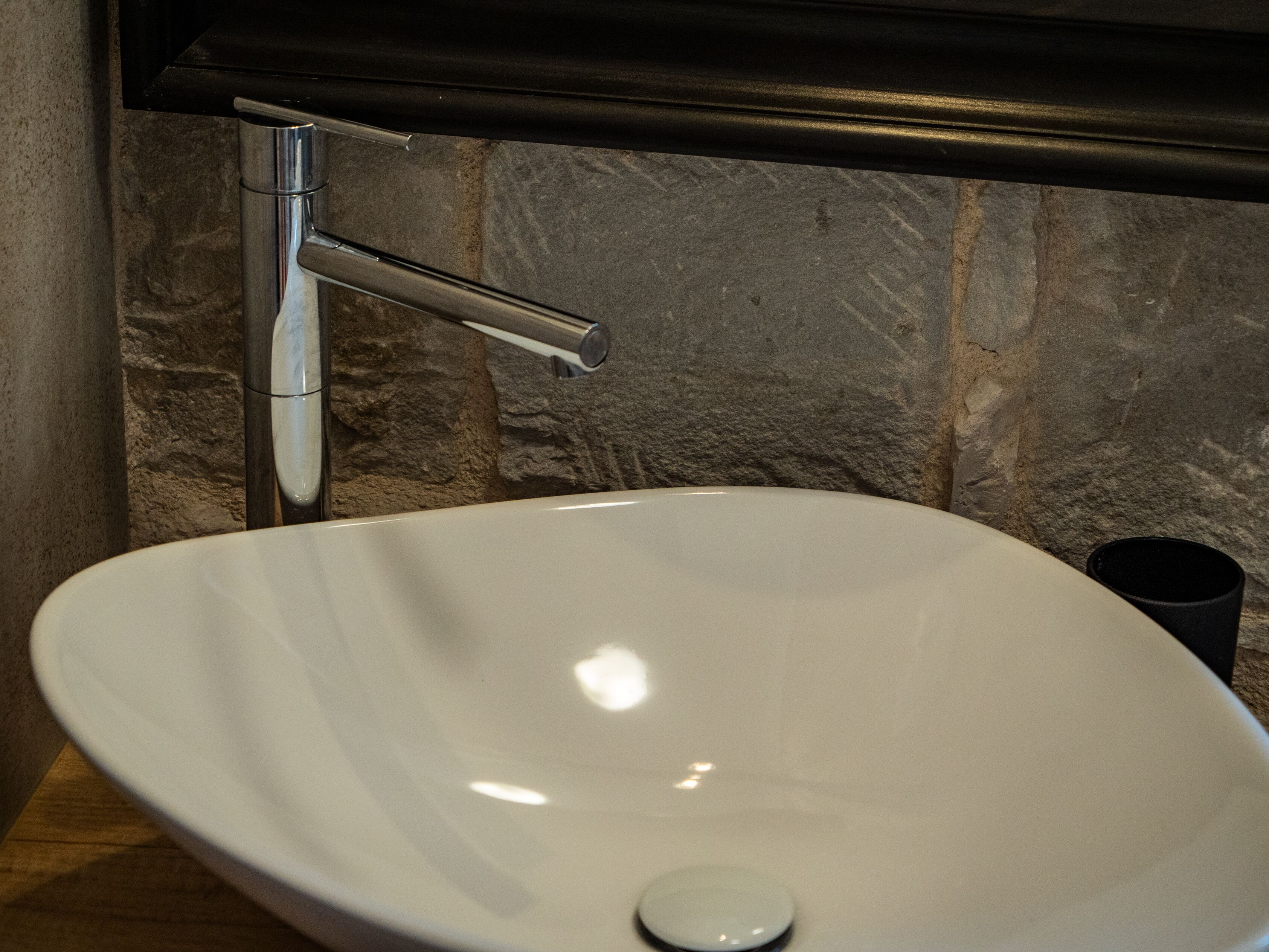 Un évier en céramique blanche, doté d’un seul robinet, est installé sur un mur en pierre à texture marquée.