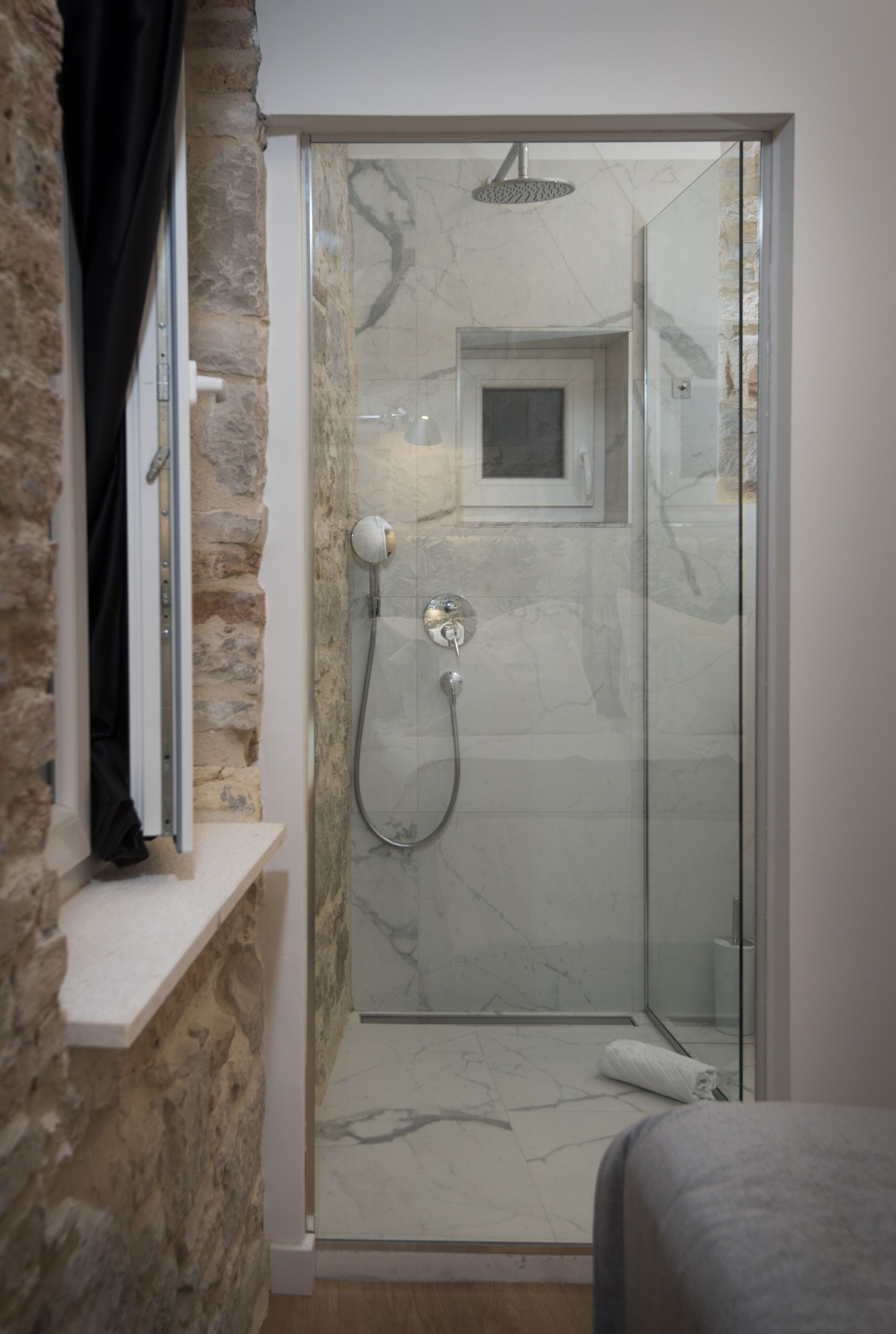 A glass-enclosed shower with a handheld showerhead and a wall-mounted faucet.