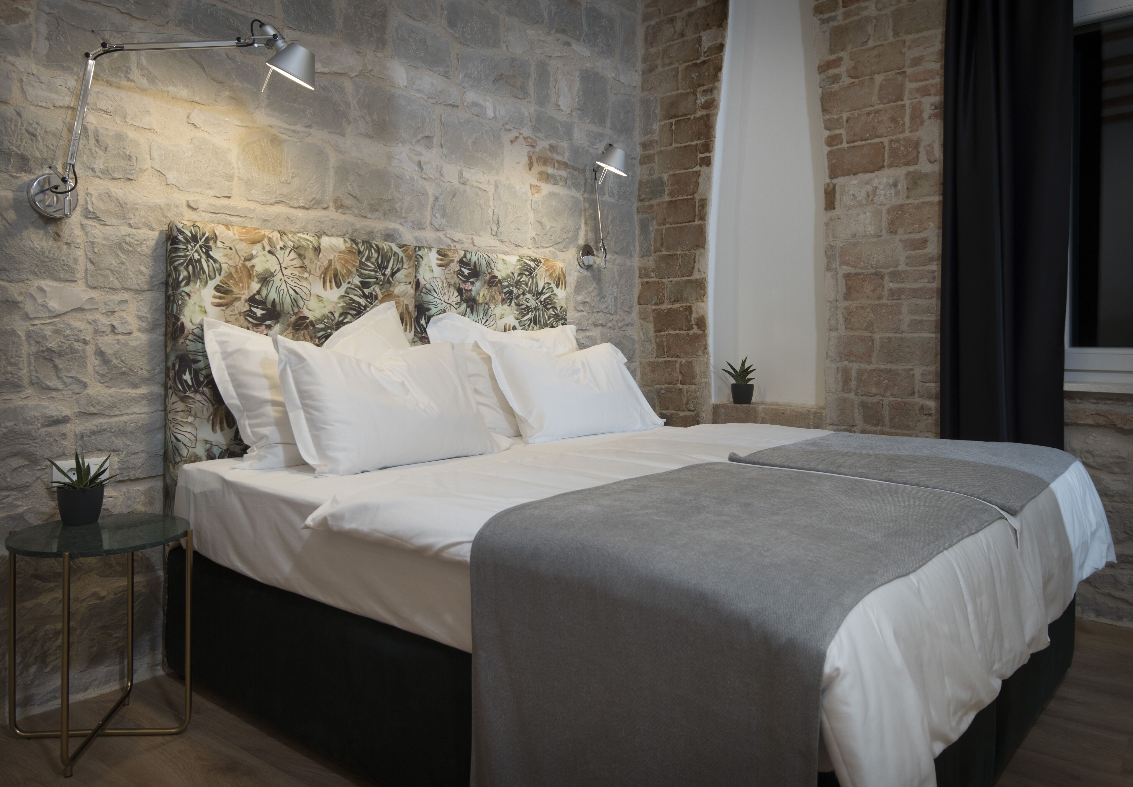 Une chambre moderne avec un mur en pierre, un grand lit recouvert de linge de maison blanc et deux lampes de chevet.