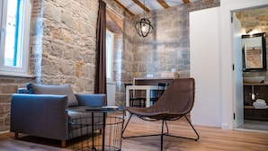 A room with stone walls, a wooden ceiling, a blue sofa, a wicker chair, a small round table, and a white door leading to a bathroom. - Emarconi history&luxury in Split center (Split)