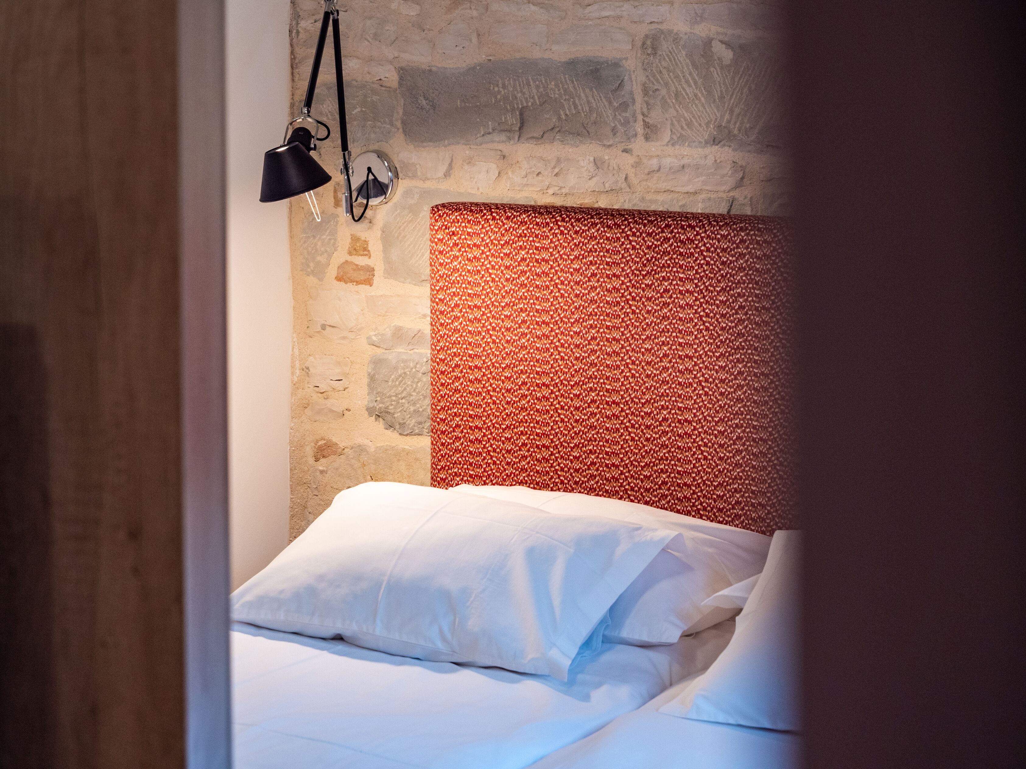 Un dormitorio con pared de piedra, cabecero estampado y cama con ropa de cama blanca.