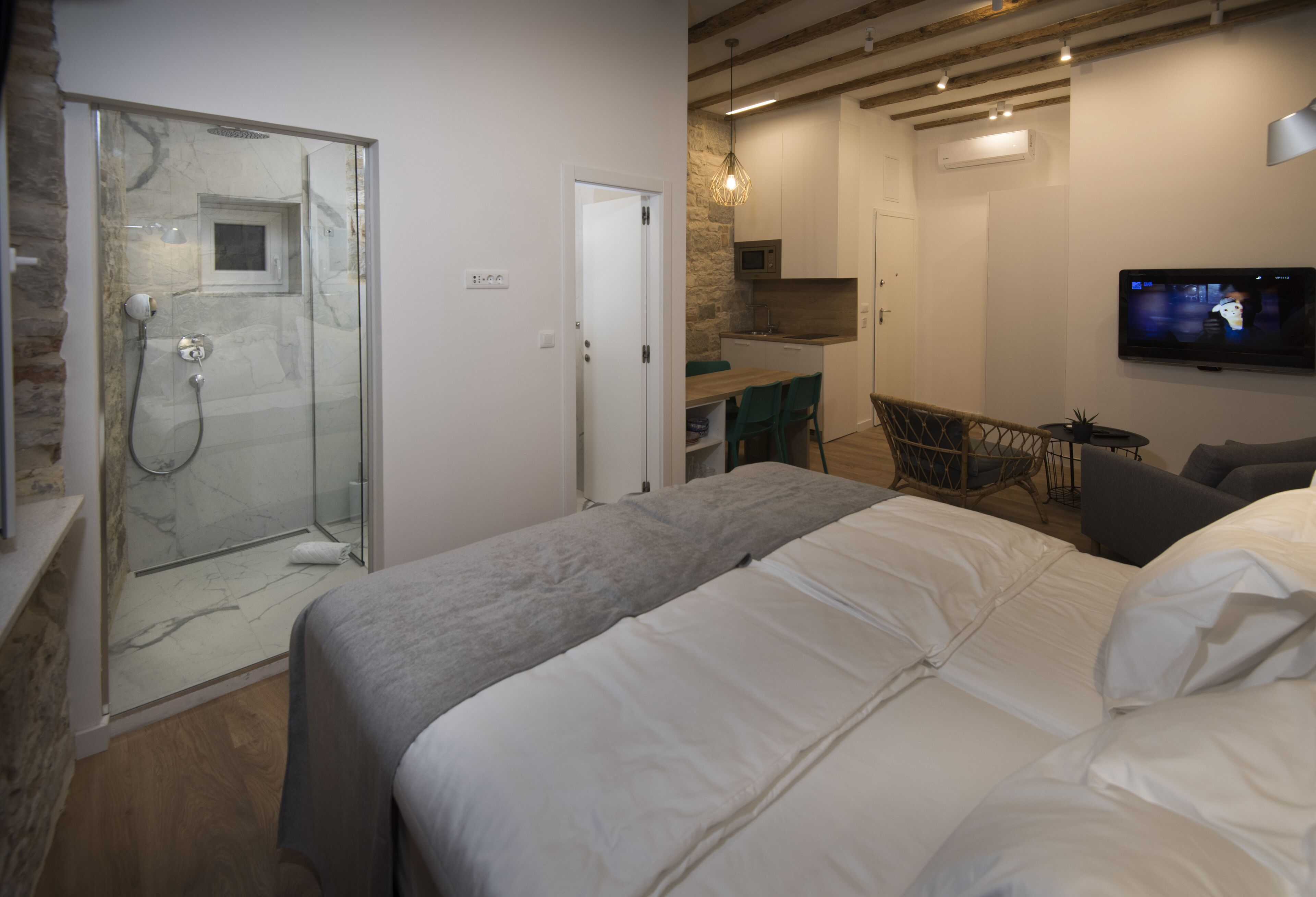 A bedroom with a bed, a shower, a dining area, and a TV.