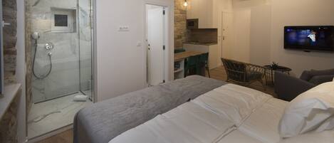 A bedroom with a bed, a shower, a dining area, and a TV.
