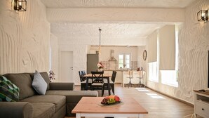 A modern living room with a sectional sofa, a wooden coffee table with fruit, a dining area with chairs, and a kitchen in the background. - Charming stone house Villa Pepina (Risika)