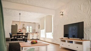 A modern living room with a wooden coffee table, a TV on a white cabinet, and a dining area with chairs and a table. - Charming stone house Villa Pepina (Risika)