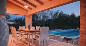 Eine Außenpatio mit Tisch und Stühlen, einem Swimmingpool und einer Ziegelsteinsäule.