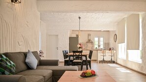 Una sala moderna con un sofá seccional, una mesa de centro de madera con fruta, una zona de comedor con sillas y una cocina al fondo.