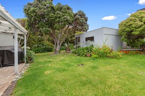 A backyard with a covered barbecue area, a small shed, and a variety of plants and flowers. - Oceans 61 Beachside Charm Ocean Views & BBQ (APOLLO BAY)
