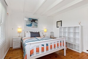 A bedroom with a white bed, bedside tables, a nightstand, a wall-mounted shelf, and a framed picture. - Oceans 61 Beachside Charm Ocean Views & BBQ (APOLLO BAY)