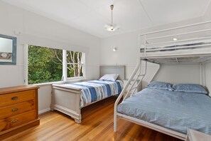 A bedroom with a bunk bed, a single bed, a dresser, and a window with a view of greenery.