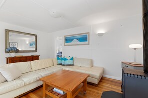 A living room with a beige sofa, a wooden coffee table, a framed picture on the wall, and a lamp. - Oceans 61 Beachside Charm Ocean Views & BBQ (APOLLO BAY)