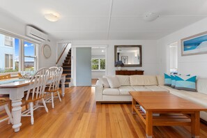 A spacious living area with a wooden dining table, white chairs, a sofa, and a wooden coffee table.