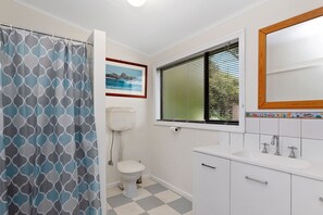 A bathroom with a toilet, a window with blinds, a shower curtain, and a sink with a mirror.