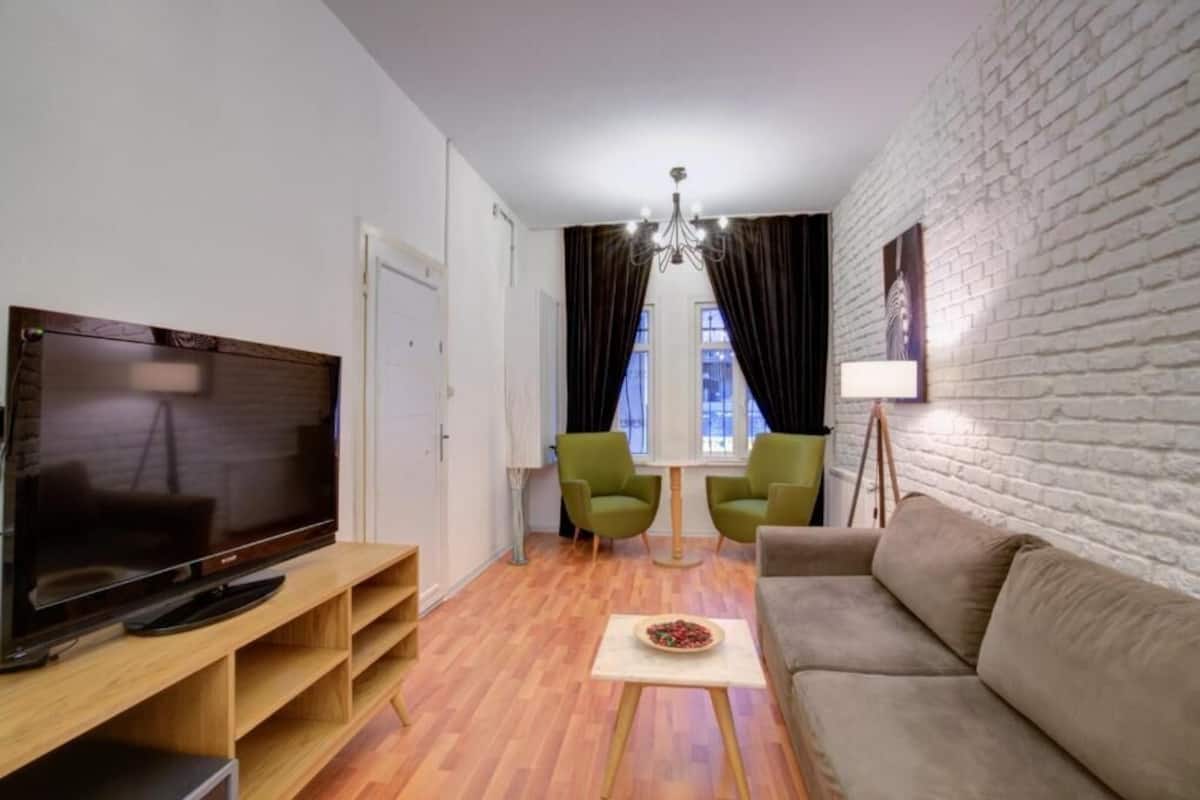 Una sala de estar moderna con televisor de pantalla plana, un sofá, una mesa de centro y un comedor con sillas.