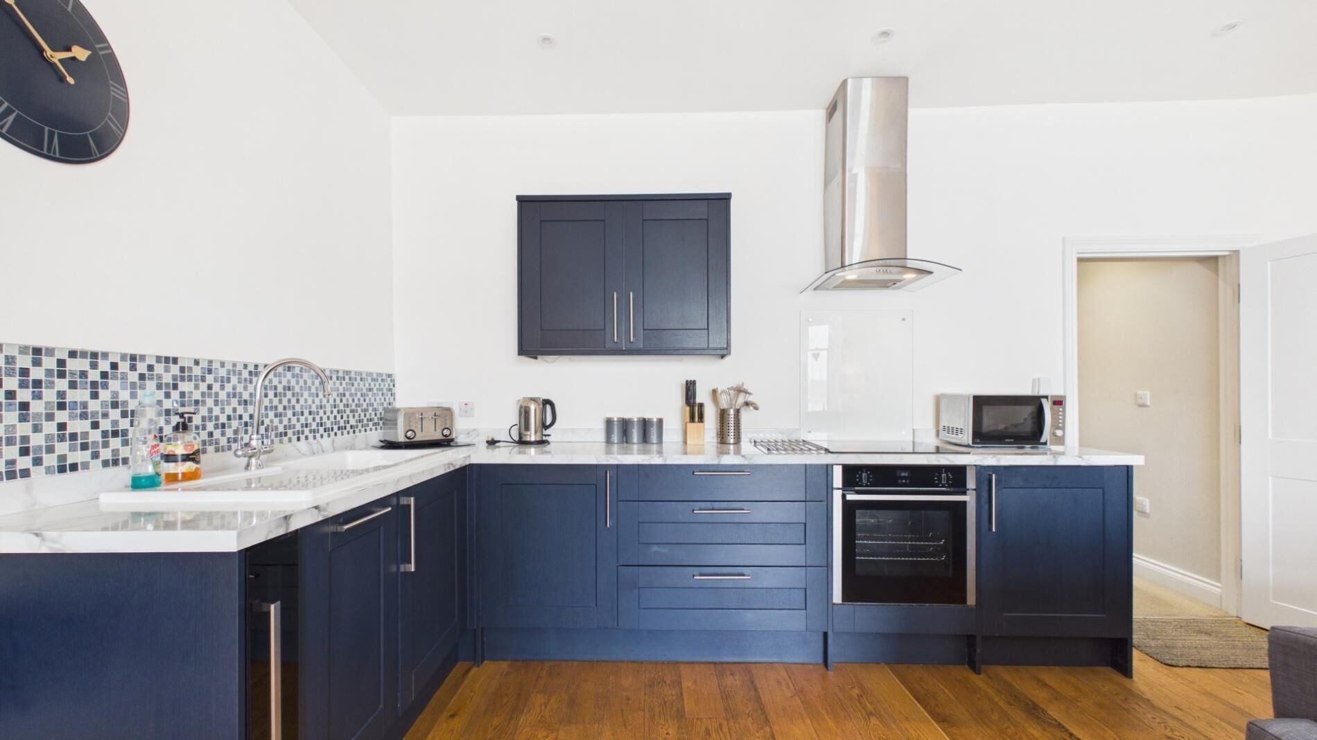 A modern kitchen with dark blue cabinets, a stainless steel range hood, a microwave, and a toaster.