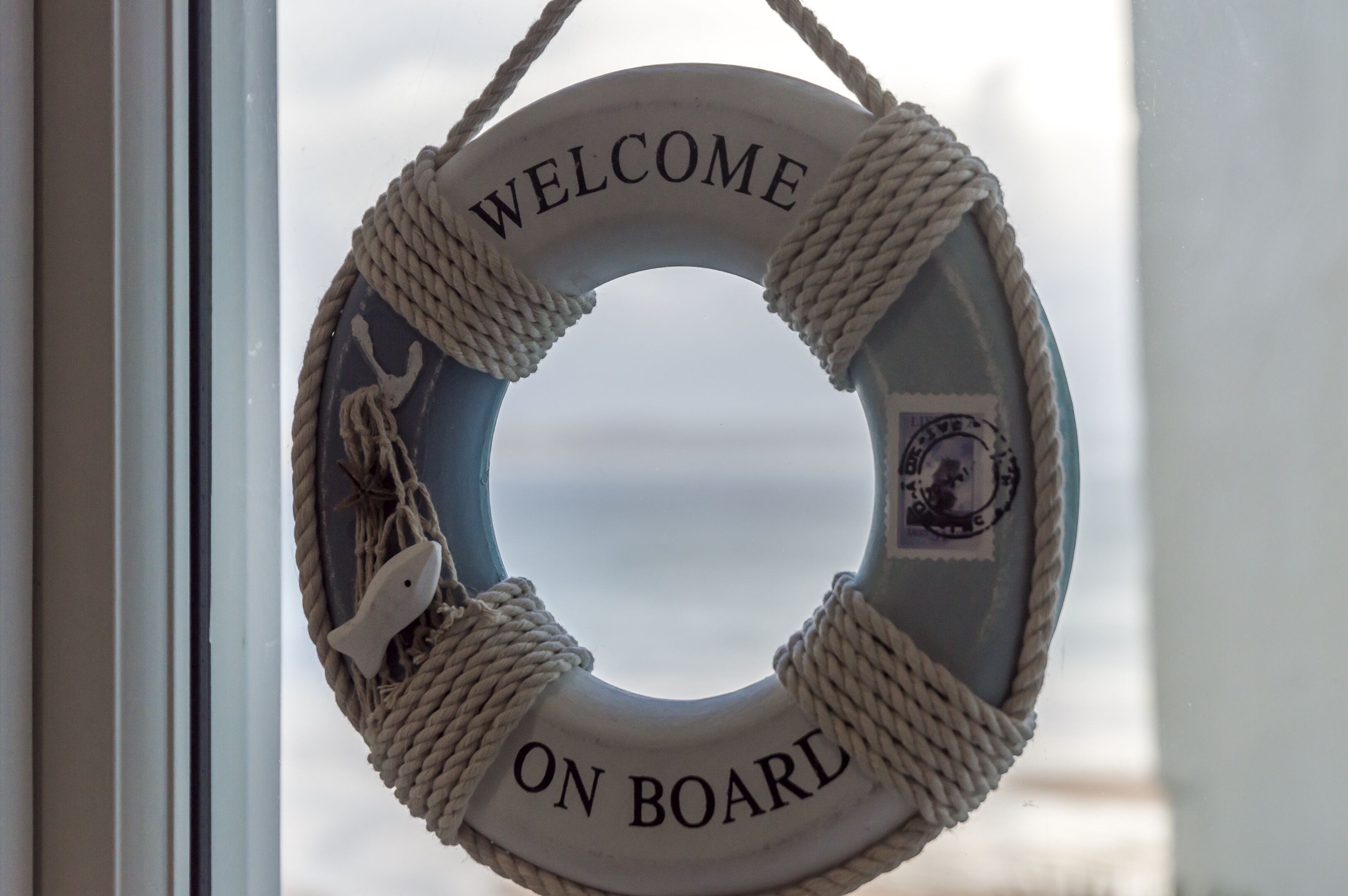 A lifebuoy with "WELCOME ON BOARD" text and a small seal, hanging by a rope.