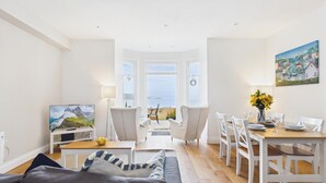 A bright living room with a dining area, a TV, and a painting. - Sea Legs (Tenby)