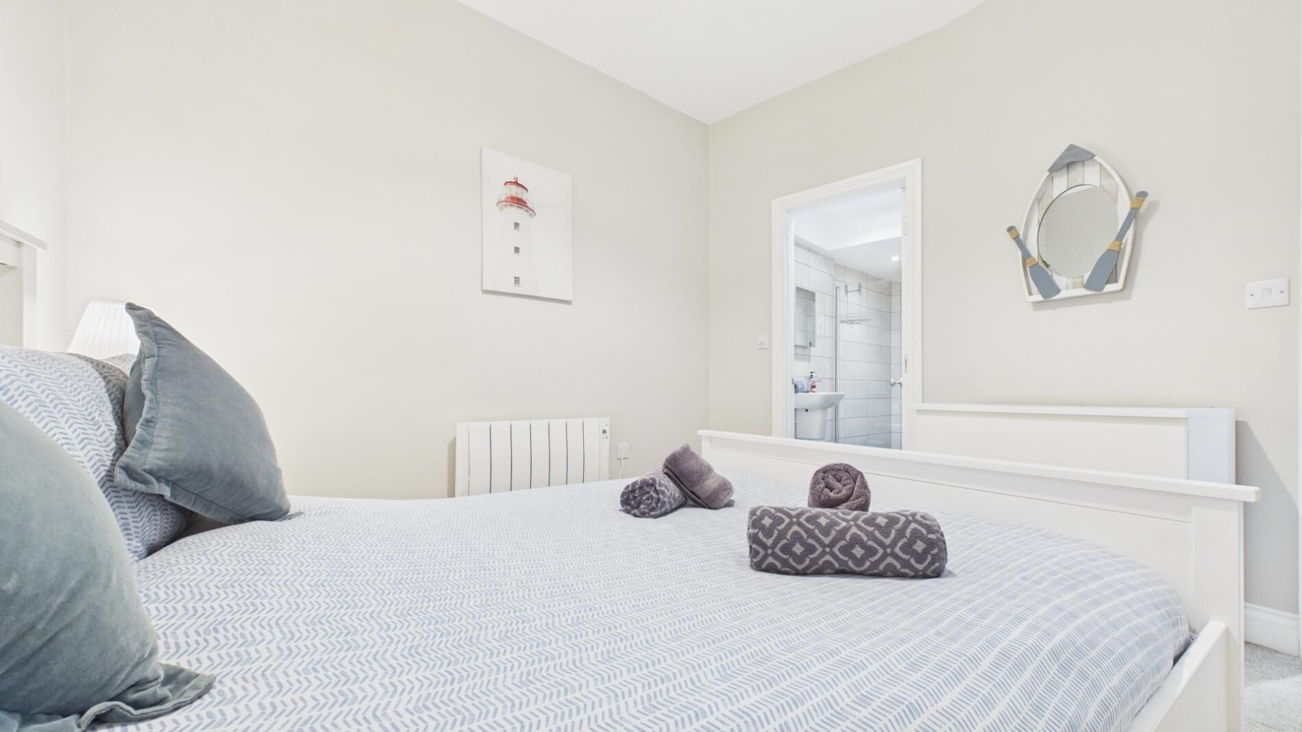 A bedroom with a bed, pillows, a radiator, a mirror, and a framed picture on the wall.
