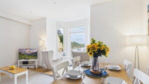 A dining area with a table set for four, a TV, and a scenic view through the window. - Sea Legs (Tenby)