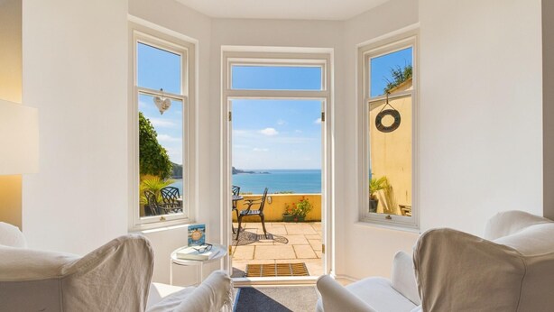 A room with a view of the sea, a door leading to an outdoor patio with a table and chairs, and a circular wall decoration. - Sea Legs (Tenby)