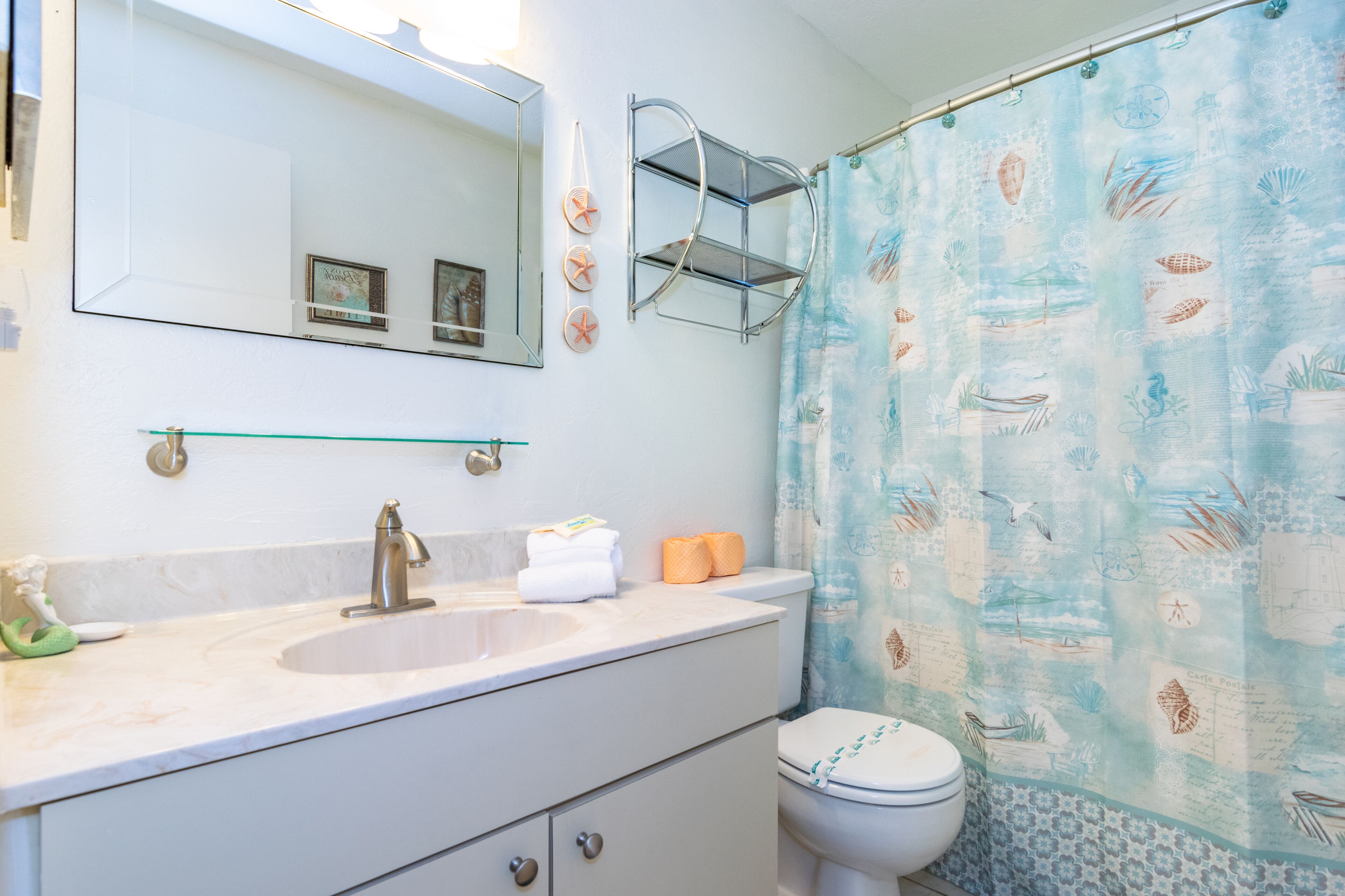 Une salle de bain avec un lavabo blanc, un miroir, des toilettes et un rideau de douche à motifs nautiques.