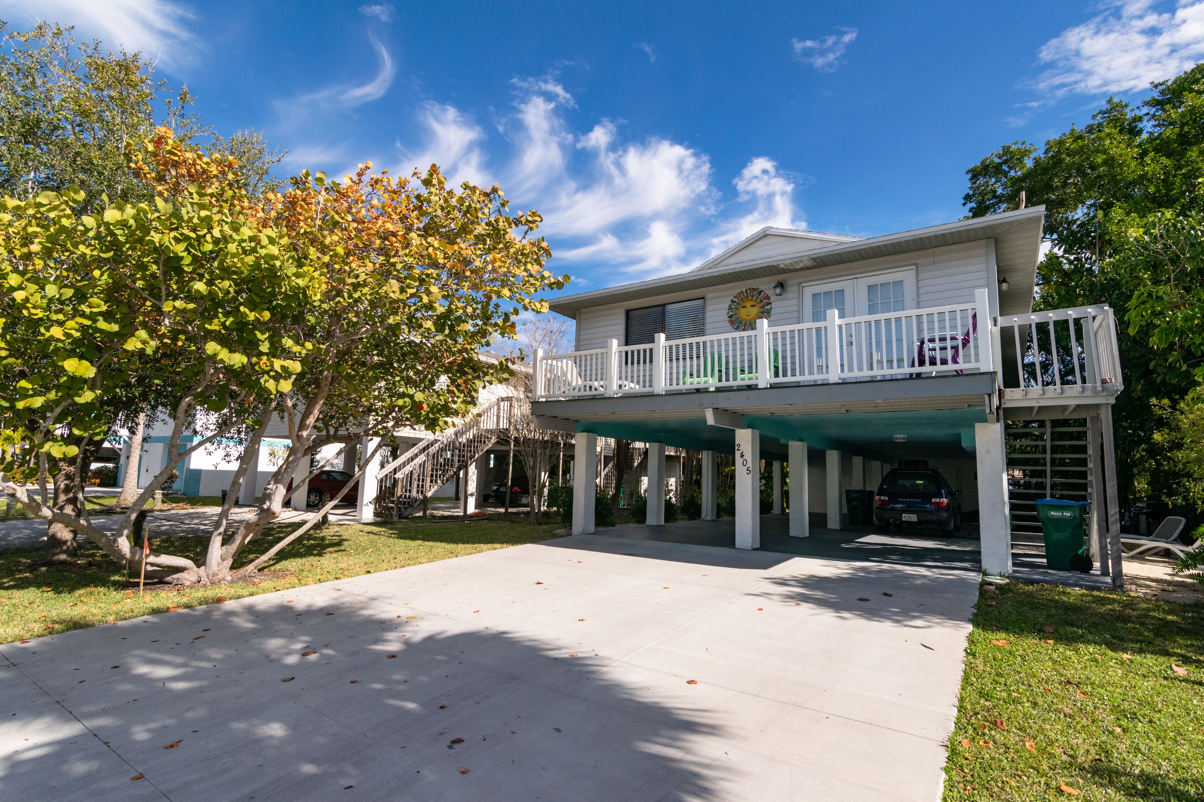A two-story house with a balcony, a covered porch, and a car parked under the house.