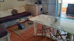 Ett kompakt bostadsutrymme med en soffa, ett litet matbord med stolar, en tvättmaskin och ett kylskåp.