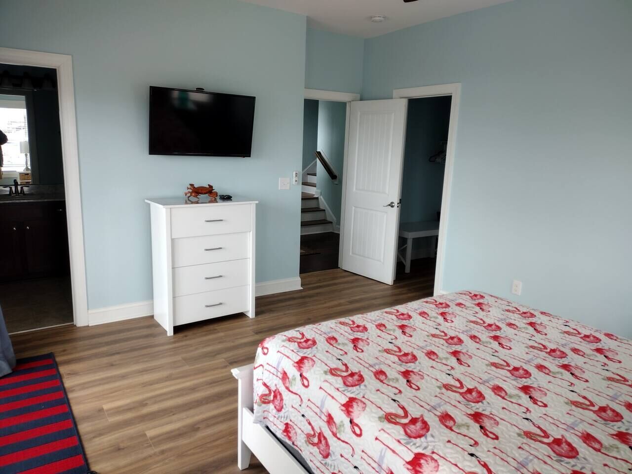 A bedroom with a bed, a dresser, a television, and a staircase leading to another room.