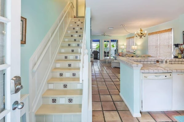 Una escalera con barandas blancas y peldaños color beige que conduce a una cocina con salpicadero de azulejos y lavavajillas empotrado.