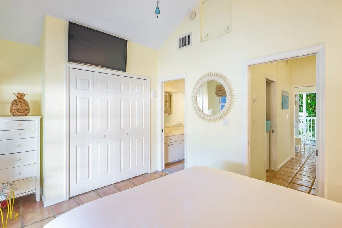 A bedroom with a bed, a wardrobe, a television, a mirror, and a door leading to a balcony.