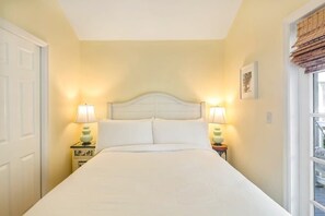 Una cama bien tendida con ropa de cama blanca, dos lámparas de noche y un cuadro en la pared.