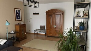 Ein Wohnzimmer mit einer Couch, einem Couchtisch, einem Schrank, einem Holzschrank, einer Pendelleuchte, einer Topfpflanze und einem Bücherregal.