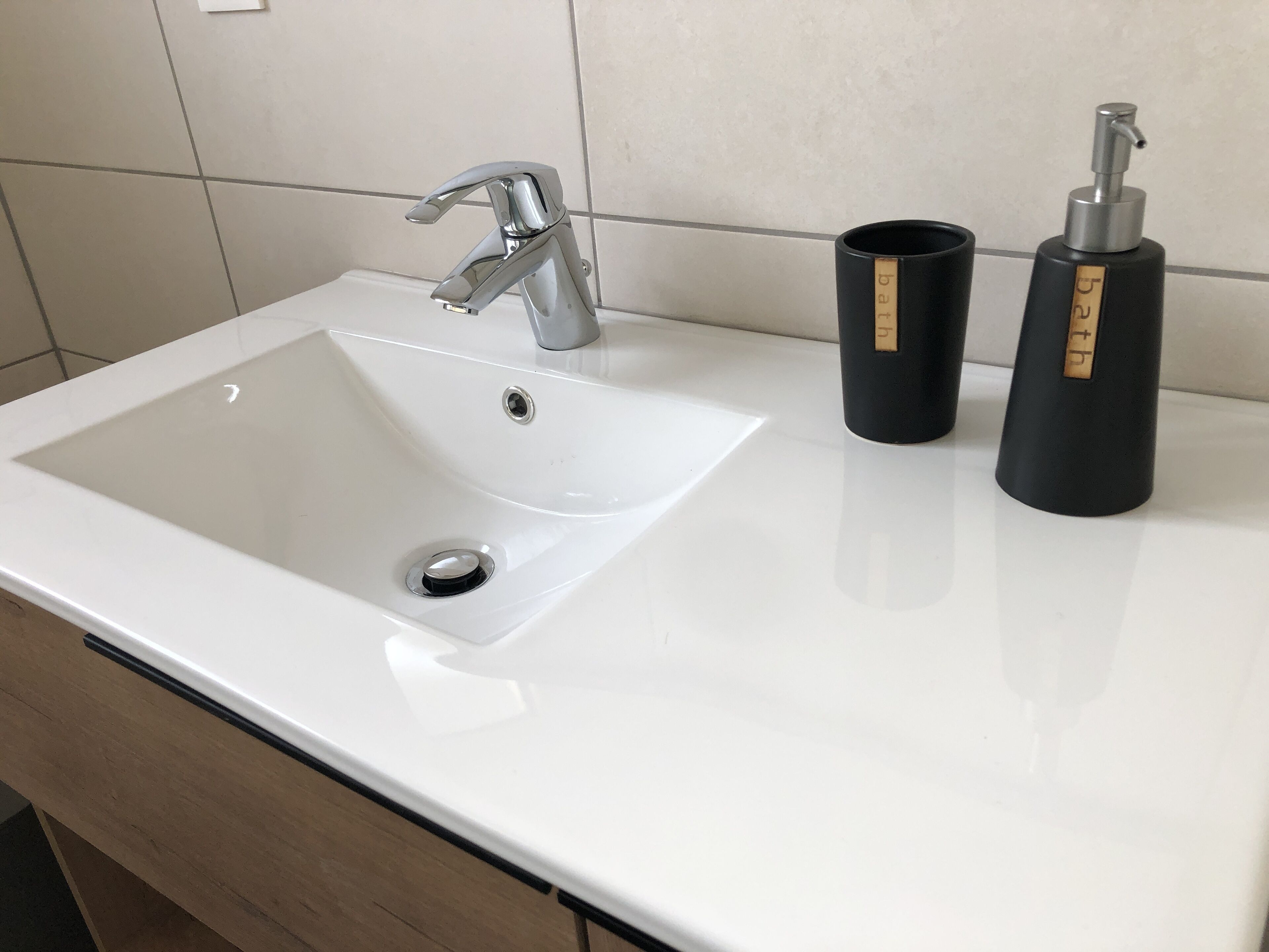 Ein weißes Waschbecken mit einem modernen Wasserhahn, zwei schwarzen Spendern und einer weißen Arbeitsplatte.