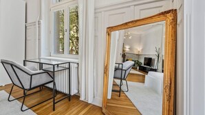Ein modernes Wohnzimmer mit einem großen Spiegel, einer Essecke mit Tisch und Stühlen sowie einem Ausblick durch ein Fenster.