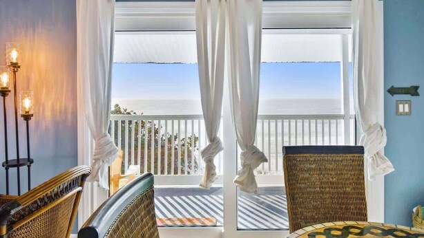 A balcony with white curtains, wicker chairs, and a table. - 3Bedroom Beachfront Condo-Gulf View-On the Sand! (Indian Rocks Beach)