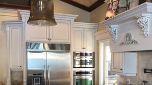 A kitchen with white cabinetry, stainless steel appliances, a marble countertop, and a hanging light fixture.