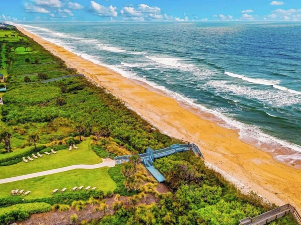 A coastal resort with a beach, a walking path, and a bridge connecting the property to the beach.
