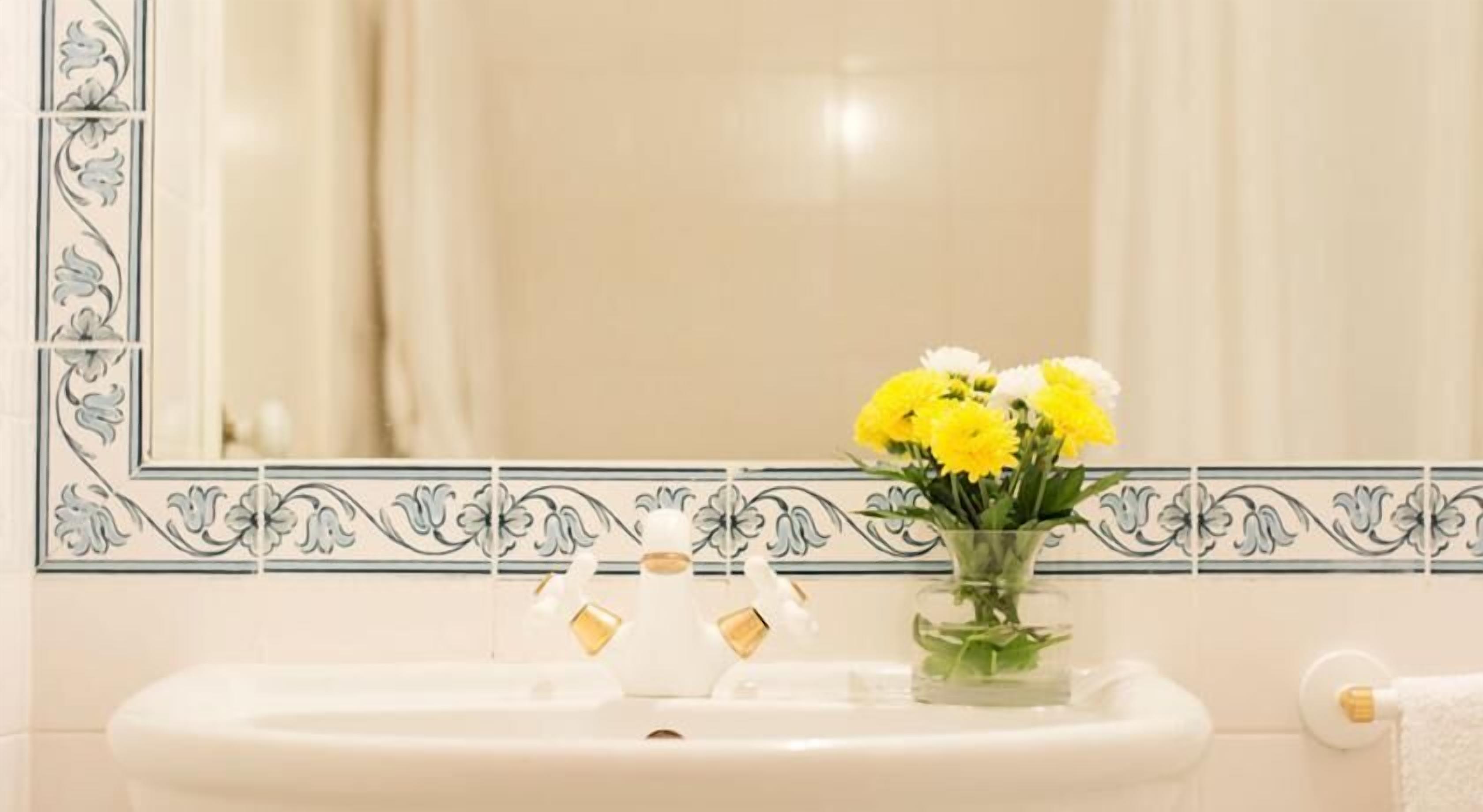 Une salle de bain avec un lavabo blanc, un miroir et un vase contenant des fleurs jaunes.