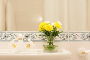 A bathroom with a white sink, a glass vase with yellow flowers, and a decorative tile backsplash. - Casa Da Piedade (São Vicente)