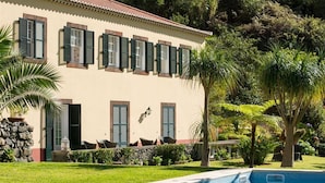 Edifici amb una piscina, envoltat de vegetació i palmeres.