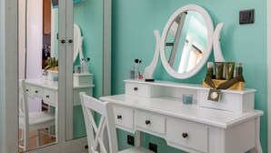 Una toeletta bianca con uno specchio grande, una sedia e uno scaffale con articoli da bagno.
