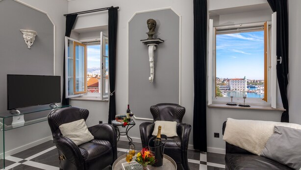 Un soggiorno moderno con due poltrone in pelle, un tavolino in vetro, una TV a schermo piatto e vista su un porto turistico.