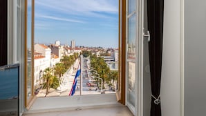 Vista dalla finestra su una città con edifici, palme e un lungomare.