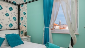 Una camera da letto con un letto, un comodino, una finestra con tende e vista sugli edifici.