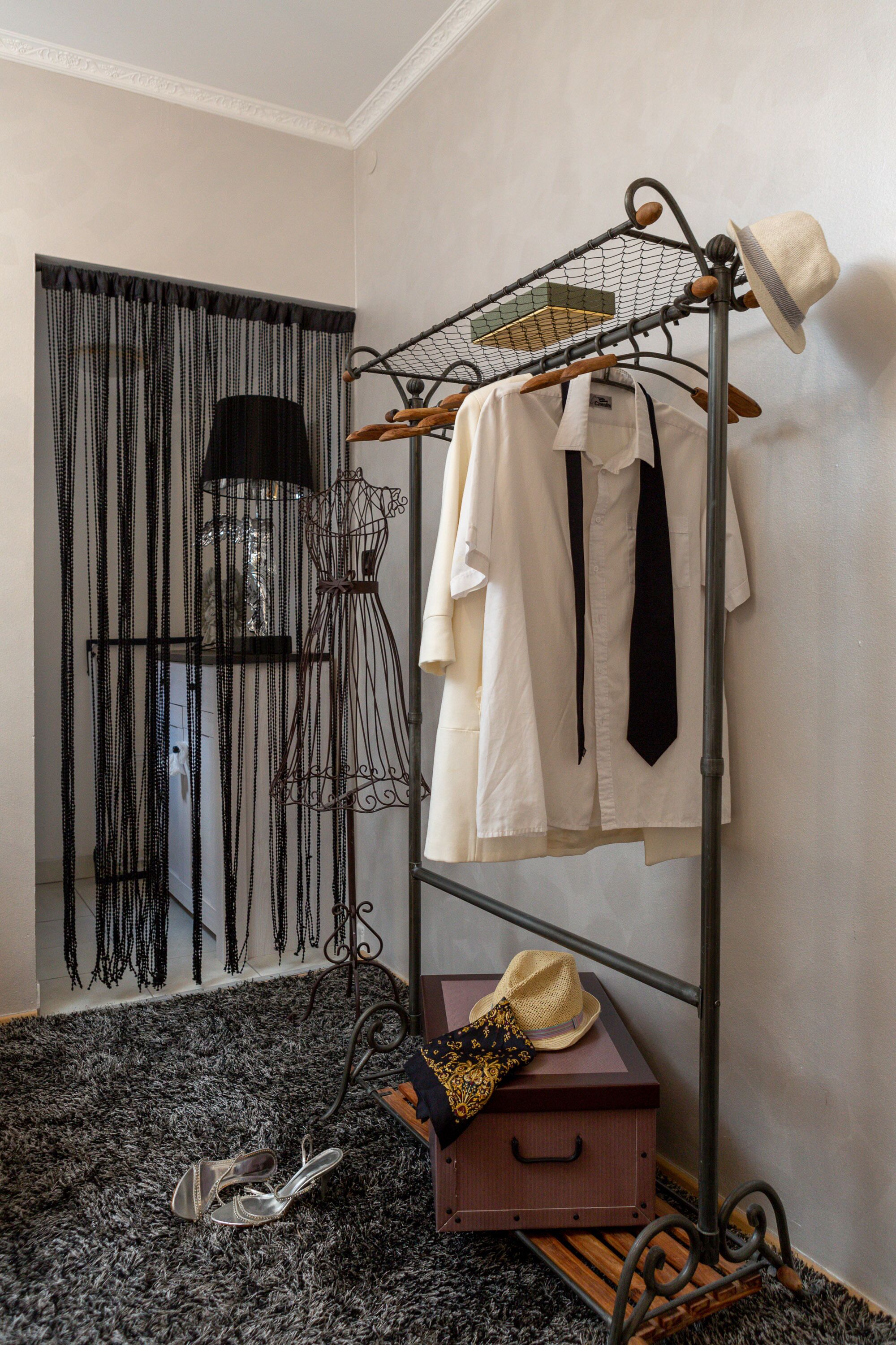 Ein Zimmer mit Kleiderstange, einer Mannequin, einem Koffer und einem Paar Schuhen auf einem gemusterten Teppich.