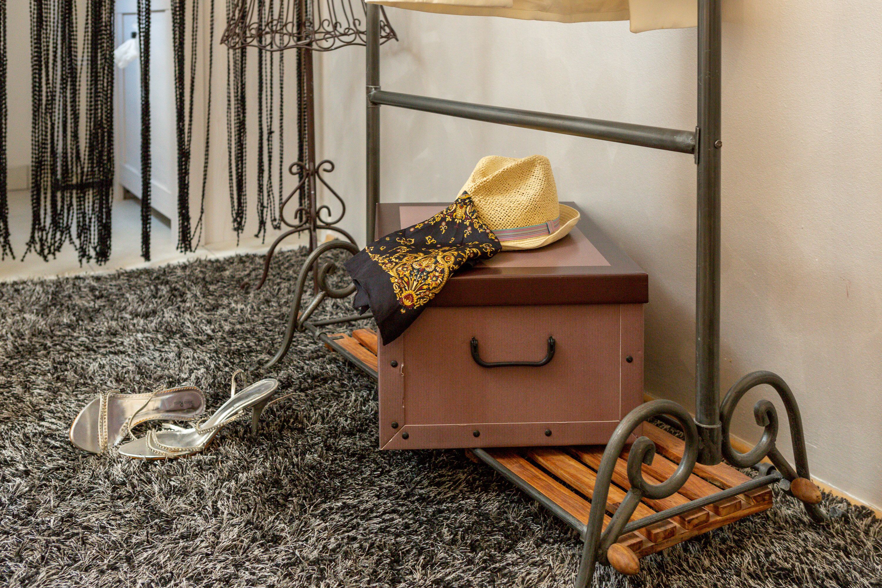 A small wooden chest with a hat and a scarf on top, placed on a metal stand with a carpeted floor.