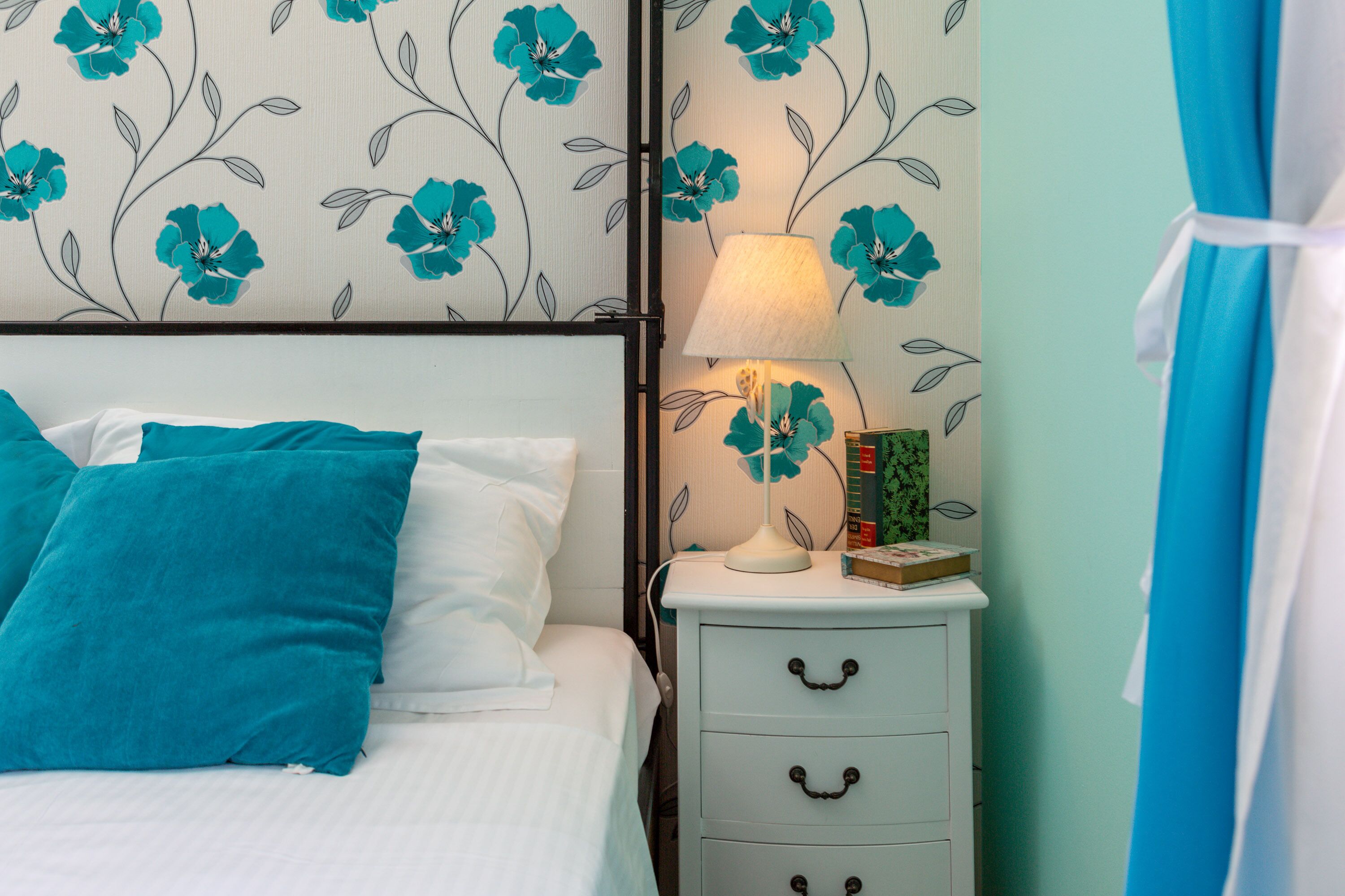 A neatly made bed with teal and white bedding, a bedside lamp, and a book on a nightstand.