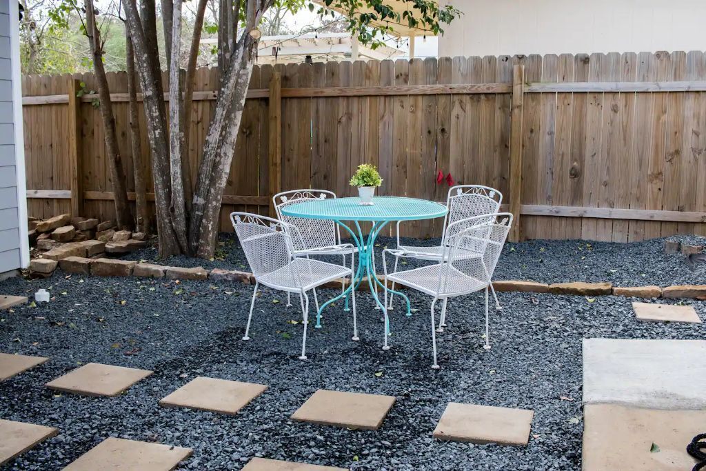 A patio with a round table and four chairs, surrounded by stepping stones and a wooden fence.